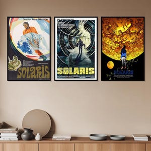 Könnte beinhalten: Drei gerahmte Filmplakate für "Solaris" werden gezeigt. Die Plakate weisen lebendige Farben und künstlerische Designs auf. Das erste Plakat zeigt eine Figur in einem orangefarbenen Hemd und eine Frau in einem weißen Kleid. Das zweite Plakat zeigt eine Figur, die einen Gang entlanggeht. Das dritte Plakat zeigt eine Figur, die eine gelbe Sonne betrachtet.
