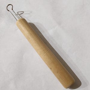 以下が含まれることがあります： 明るい木製のハンドルと、端に銀色の金属ループが付いたツール。ハンドルは円筒形です。このツールは、詳細な作業や工芸に使用される可能性があります。ループはワイヤー製です。