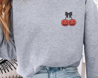 Puede incluir: Una sudadera gris jaspeado con un pequeño diseño bordado de dos calabazas sonrientes y un lazo negro. La parte superior de manga larga está hecha de un material suave, adecuada para uso casual.