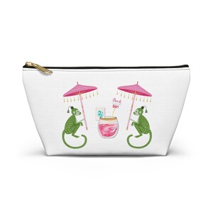 May include: White cosmetic bag with a gold zipper. The bag features a whimsical illustration of two green monkeys under pink parasols, with a cocktail and the text "Beach Bam".