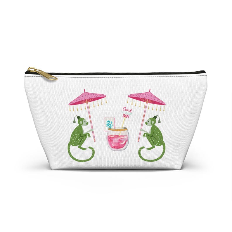 May include: White cosmetic bag with a gold zipper. The bag features a whimsical illustration of two green monkeys under pink parasols, with a cocktail and the text "Beach Bam".