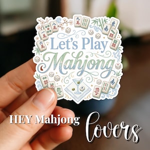 May include: A sticker with the text "Let's Play Mahjong" in blue and green script, surrounded by illustrations of mahjong tiles, dice, and a martini. The sticker also includes the text "HEY Mahjong lovers" in a handwritten font.