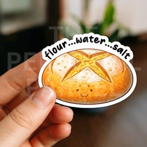 May include: A sticker featuring a cartoon loaf of bread with a smiling face. The bread is golden brown with a cross-shaped design on top. The text "flour...water...salt" is above the bread.