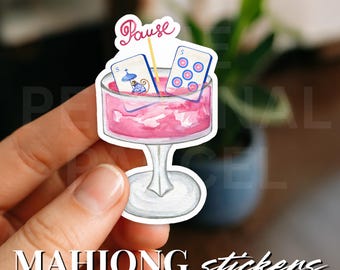 May include: A sticker featuring a pink cocktail glass with two Mahjong tiles and a "Pause" banner. The sticker has the words "MAHJONG stickers" at the bottom.