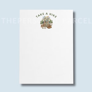 May include: A white notepad featuring a centered illustration of a hiking backpack, brown boots, a wooden signpost, and pine trees, topped with the text "TAKE A HIKE" in green lettering. The design includes small colorful wildflowers and a compass.