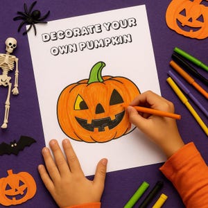 May include: A child's hands coloring a pumpkin drawing with an orange marker. The drawing is on a white sheet of paper with the text "DECORATE YOUR OWN PUMPKIN". Halloween-themed decorations, including a skeleton, spider, and felt pumpkin, are scattered around.
