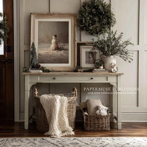 May include: A vintage-inspired interior scene featuring a console table adorned with framed artwork, a wreath, and decorative items. Woven baskets hold a blanket and pillows. The scene evokes a cozy, rustic aesthetic, perfect for home decor.