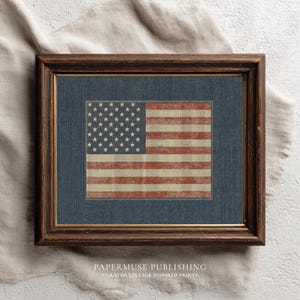 May include: Framed print of the American flag with a distressed, vintage look. The flag features red and white stripes and a field of white stars on a blue background. The print is set in a dark brown wooden frame.