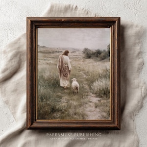 May include: A framed print depicting a figure in a robe walking with a lamb on a path through a field. The artwork has a vintage aesthetic with muted tones and is set in a dark brown wooden frame. The text "PAPERMUSE PUBLISHING" and "CURATED VINTAGE INSPIRED PRINTS" is at the bottom.
