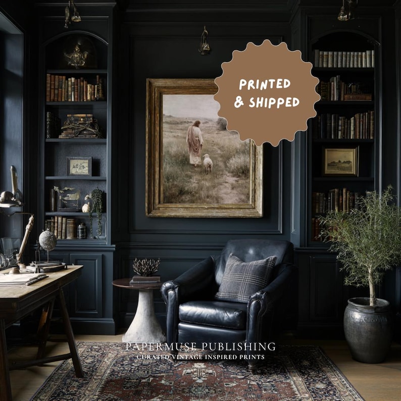 May include: A dark, moody room with built-in bookshelves, a leather armchair, and a framed vintage print. The print depicts a figure with a lamb in a field. The text "PRINTED & SHIPPED" is on a brown circular sticker. The text "PAPERMUSE PUBLISHING CURATED VINTAGE INSPIRED PRINTS" is at the bottom.
