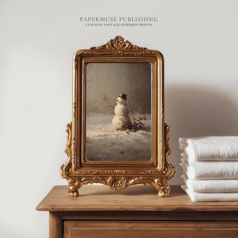 May include: A framed vintage print of a snowman in a snowy landscape. The ornate gold frame features intricate detailing. The text "PAPERMUSE PUBLISHING CURATED VINTAGE INSPIRED PRINTS" is at the top of the frame.