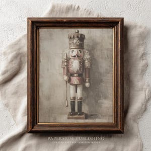 Puede incluir: Una impresión enmarcada de un soldado cascanueces vintage. El cascanueces está pintado en tonos de rojo, blanco y negro, con una corona y un bigote detallados. El marco es de color marrón oscuro. El texto "PAPERMUSE PUBLISHING" es visible en la parte inferior.