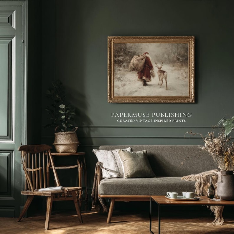 Puede incluir: Una impresi&oacute;n vintage enmarcada que representa una figura con abrigo rojo y un ciervo en un paisaje nevado. La impresi&oacute;n cuelga sobre un sof&aacute; gris con cojines decorativos. El texto "PAPERMUSE PUBLISHING CURATED VINTAGE INSPIRED PRINTS" est&aacute; debajo.