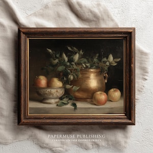 Op de afbeelding: Een ingelijst vintage stilleven schilderij met een koperen pot vol groene bladeren, een decoratieve kom met appels en losse appels. Het schilderij heeft een donkere achtergrond en is gesigneerd door Papermuse Publishing.