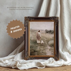 May include: Framed print featuring a vintage-inspired image of a figure walking with a lamb in a field. The print is in a dark brown ornate frame with gold accents. The text "PAPERMUSE PUBLISHING CURATED VINTAGE INSPIRED PRINTS" is at the top. A brown sticker says "PRINTED & SHIPPED".
