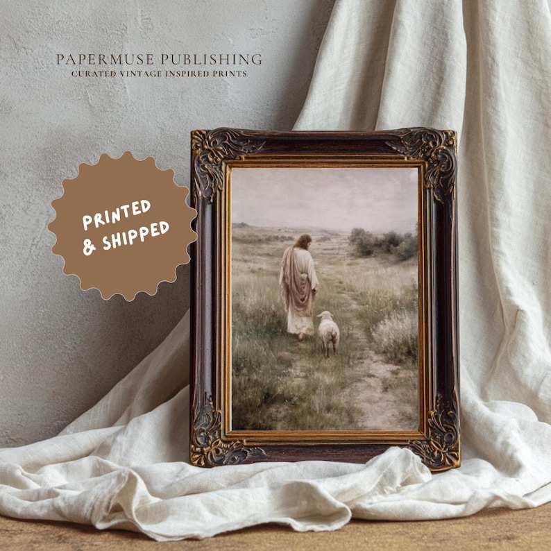 May include: Framed print featuring a vintage-inspired image of a figure walking with a lamb in a field. The print is in a dark brown ornate frame with gold accents. The text "PAPERMUSE PUBLISHING CURATED VINTAGE INSPIRED PRINTS" is at the top. A brown sticker says "PRINTED & SHIPPED".