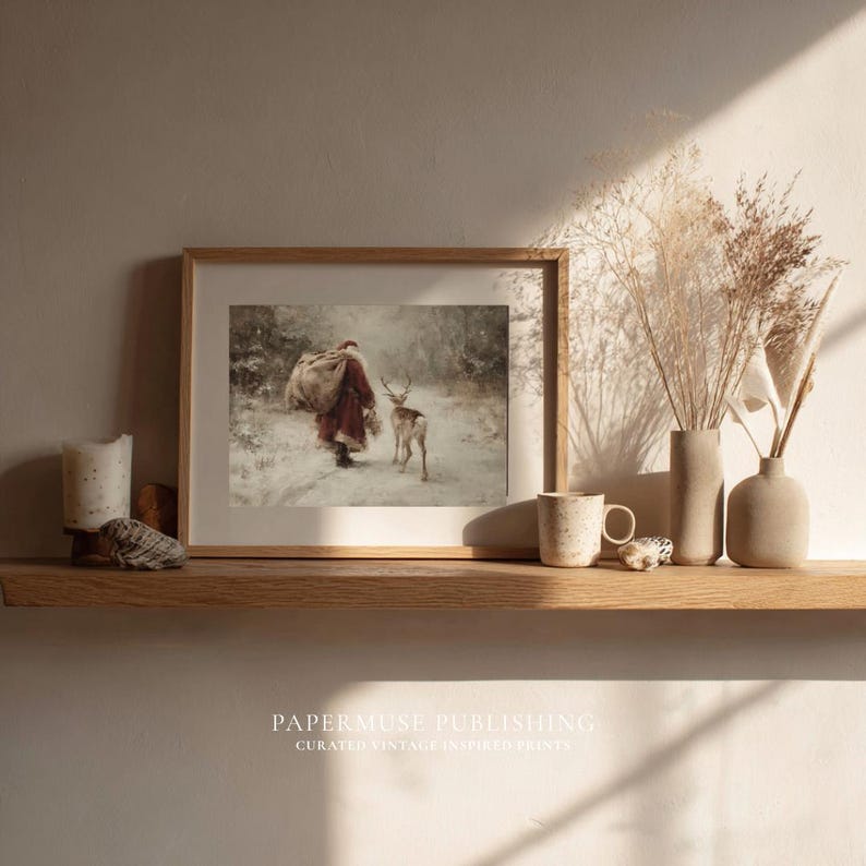 Puede incluir: Una impresi&oacute;n enmarcada muestra a Pap&aacute; Noel caminando con un ciervo en un bosque nevado. La impresi&oacute;n est&aacute; en un marco de madera clara y descansa sobre una repisa de madera con jarrones decorativos, una vela y una taza. El texto "PAPERMUSE PUBLISHING" est&aacute; abajo.