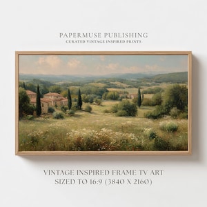 May include: A framed landscape print featuring a vintage-inspired painting of a Tuscan countryside. The artwork depicts rolling hills, trees, and buildings under a cloudy sky. The frame is made of light-colored wood.