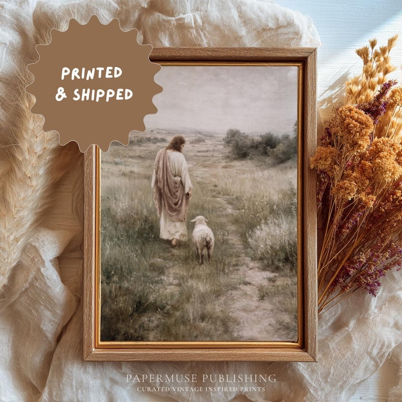 May include: Framed print of a religious scene depicting a figure in a robe walking with a lamb on a grassy path. The artwork is in a wooden frame. The text "PRINTED & SHIPPED" is in a brown circle. The bottom of the frame has the text "PAPERMUSE PUBLISHING".