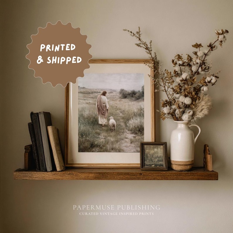 May include: A framed print of a religious figure with a lamb, displayed on a wooden shelf with books and a vase of dried flowers. The print is in a light-colored frame. The text "PRINTED & SHIPPED" is in a brown circle. The text "PAPERMUSE PUBLISHING" is below the shelf.
