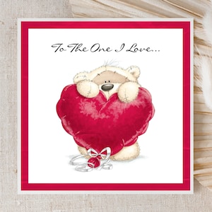 Peut inclure: Carte de vœux avec un ours en peluche tenant un grand cœur rouge. La carte a un fond blanc avec un bord rouge. Le texte "To The One I Love..." est en haut. Un ruban argenté et un ornement de cœur rouge sont en bas.