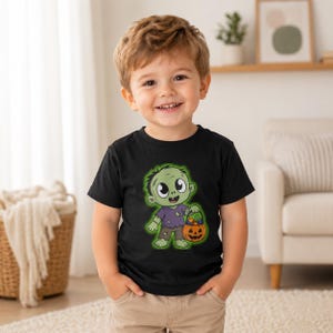 Puede incluir: Una camiseta negra de manga corta con el gráfico de un zombi de dibujos animados de piel verde, que lleva una camisa morada desgarrada y pantalones marrones, sosteniendo un cubo de calabaza naranja lleno de dulces coloridos sobre un brillo verde.