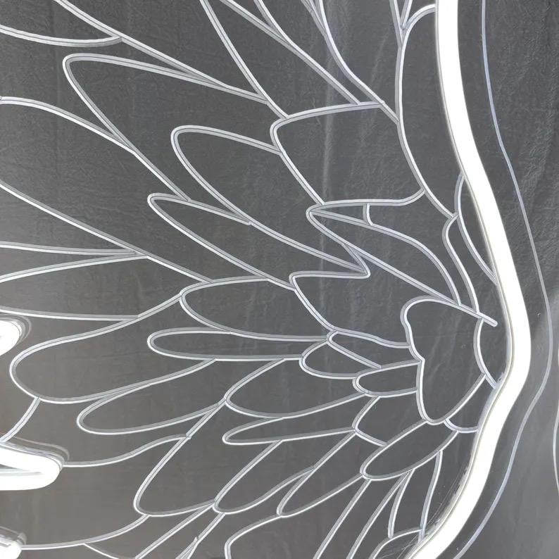 May include: A clear acrylic panel featuring a detailed laser-etched design of large, layered bird wings. The etched lines are white and create a high-contrast pattern against the transparent surface, showing individual feathers in a fan-like arrangement.