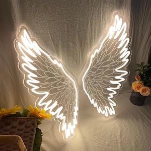 May include: A bright white LED neon sign shaped like a pair of large, detailed angel wings. The wings feature intricate feather outlines and emit a soft, glowing light, creating a distinct silhouette against the textured fabric backdrop.