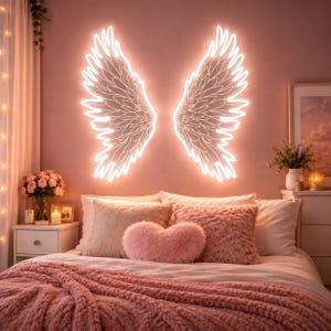 May include: A pair of glowing white neon angel wings mounted on a wall above a bed. The wings feature detailed feather outlines and emit a bright light, positioned symmetrically over a bed with pink pillows and a textured pink throw blanket.