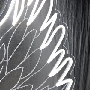 May include: A white LED neon sign shaped like a large wing, featuring bright white light tubes mounted on a clear acrylic backing with etched feather details that follow the curved outline of the wing structure.