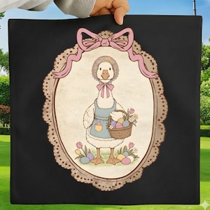 Könnte beinhalten: Ein schwarzes quadratisches Kissen mit einer Vintage-Illustration einer Gans mit Häubchen und Schürze, die einen Korb mit Ostereiern und Blumen trägt. Das Bild ist mit einer rosa Schleife und einem dekorativen ovalen Rahmen versehen.