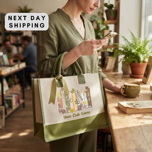A woman is standing in a bookstore, holding a bag with a printed design of books and flowers, and looking at her phone.