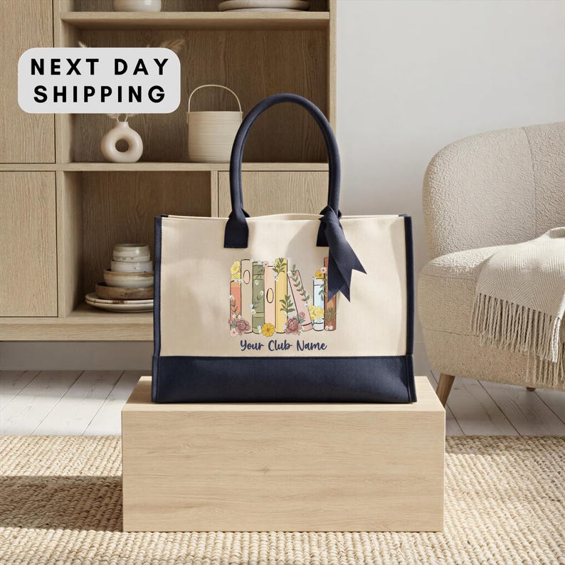 A beige tote bag with a floral design and the text "Your Club Name" printed on it, placed on a wooden box.