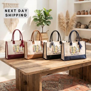four tote bags with printed designs, arranged on a wooden table. The bags are of different colors and sizes, and they appear to be made of canvas or leather. The background features a beige wall with a hanging plant and shelves displaying various decorative items.