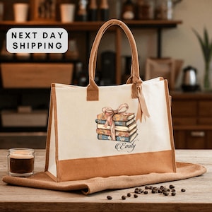 May include: Cream-colored tote bag with brown accents and handles. The bag features a stack of books with a pink ribbon and the name "Emily" printed below. The words "NEXT DAY SHIPPING" are in a white box in the upper left corner.
