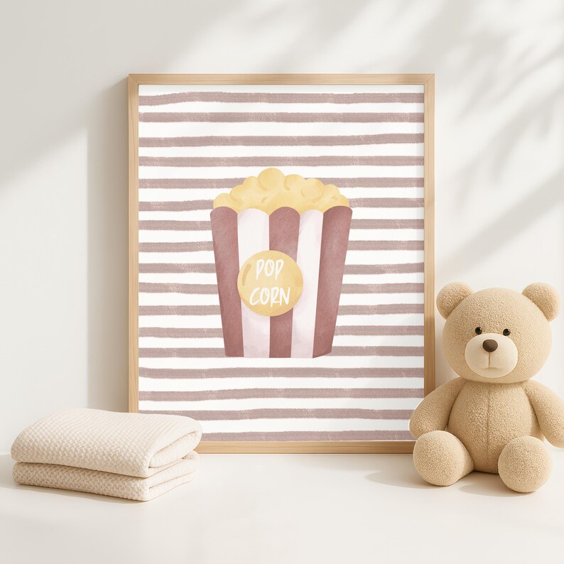 Pode incluir: Impress&atilde;o emoldurada com uma ilustra&ccedil;&atilde;o de pipocas. O recipiente de pipocas &eacute; vermelho e branco com um c&iacute;rculo amarelo que diz "Pop Corn". O fundo tem listras horizontais marrons e brancas. Um urso de pel&uacute;cia e um cobertor dobrado est&atilde;o na imagem.