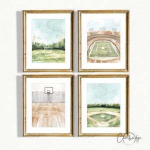以下が含まれることがあります： スポーツフィールドを描いた、額装された4つの水彩画プリント。プリントは、サッカー場、フットボールスタジアム、バスケットボールコート、野球場を描いています。各プリントは金色のフレームで、緑、茶色、青の色合いの水彩画スタイルです。