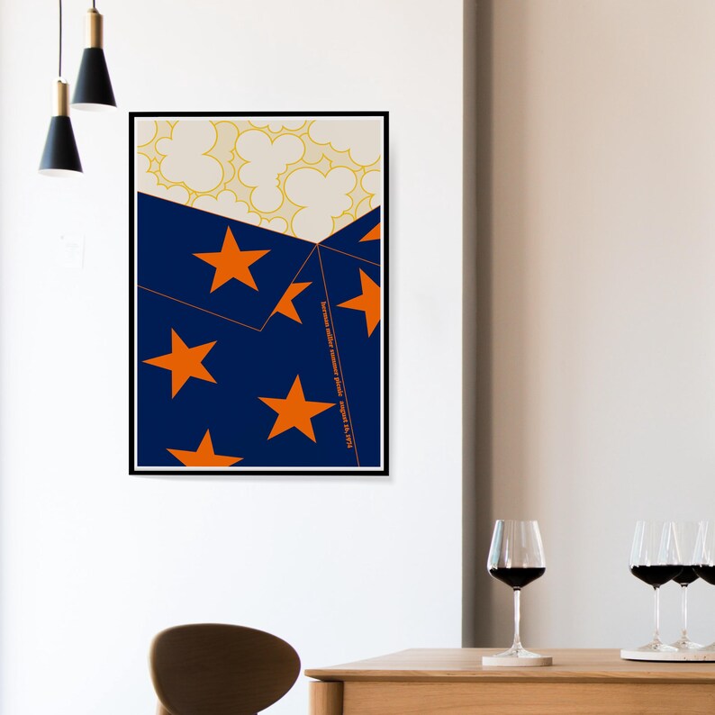 May include: A framed art print with a geometric design. The artwork features a navy blue section with orange stars, a cream section with yellow cloud shapes, and vertical text. The print is displayed on a white wall, with wine glasses in the foreground.