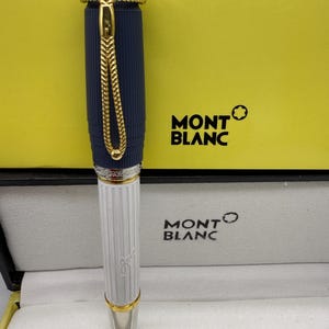 Pu&ograve; includere: Una penna Montblanc con un corpo blu navy e una sezione inferiore bianca. La penna presenta dettagli color oro e una catena decorativa. La penna &egrave; presentata in una scatola Montblanc con il logo del marchio.