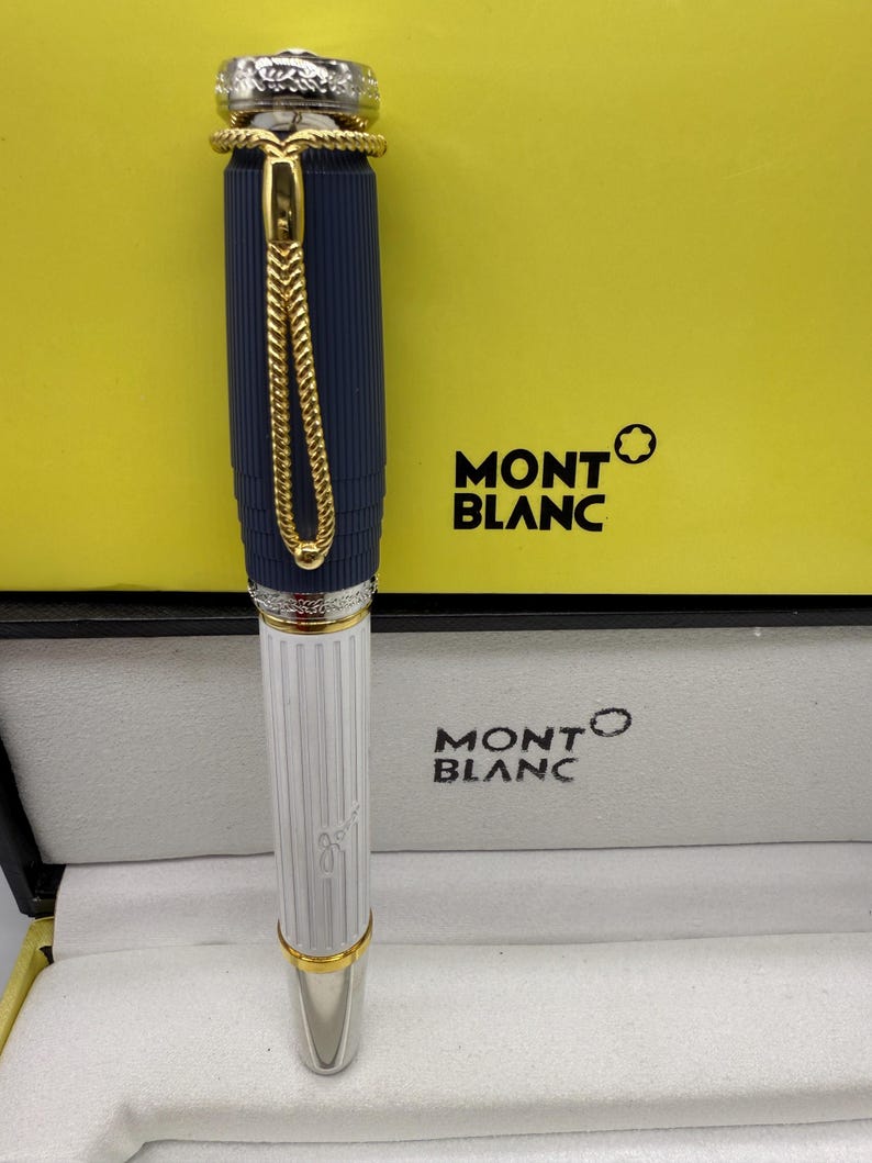 Pu&ograve; includere: Una penna Montblanc con un corpo blu navy e una sezione inferiore bianca. La penna presenta dettagli color oro e una catena decorativa. La penna &egrave; presentata in una scatola Montblanc con il logo del marchio.