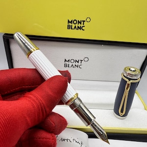 Pu&ograve; includere: Una penna stilografica Montblanc con corpo bianco e dettagli argentati, presentata in una scatola gialla e bianca. La penna ha un pennino dorato ed &egrave; visibile un libretto con la scritta "The art of writing".