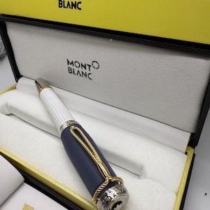 Pu&ograve; includere: Una penna Montblanc in una scatola gialla e nera. La penna ha un corpo bianco e blu navy con dettagli dorati. La penna &egrave; in una scatola foderata bianca con il logo Montblanc. La scatola &egrave; all'interno di una scatola gialla con il logo Montblanc.