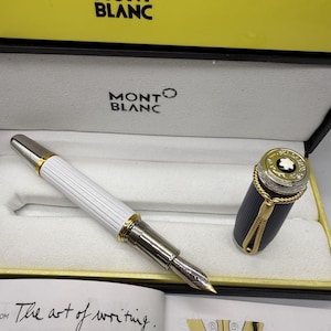 Pu&ograve; includere: Una penna stilografica Montblanc nella sua scatola di presentazione. La penna ha un fusto bianco e scanalato con dettagli dorati e argentati. Il cappuccio &egrave; staccato, rivelando un design nero e oro. La scatola &egrave; gialla e bianca con il logo Montblanc.