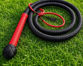 May include: A braided whip featuring a long black cord coiled in a circle, a bright red handle section, and a round black knot at the base. A red wrist loop is attached near the top of the handle, featuring a small black tassel detail.