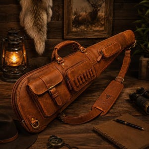 Puede incluir: Un estuche para rifle de cuero marrón con asa superior, correa ajustable para el hombro con un logotipo de toro y múltiples bolsillos exteriores. El estuche incluye un bolsillo grande con hebilla y un bolsillo pequeño con cremallera y trabillas.