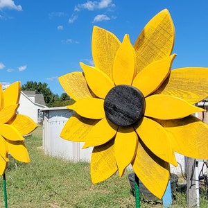 May include: Two large yellow wooden sunflowers with black centres on green metal stakes in a grassy yard.