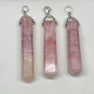 May include: Three pink quartz crystal pendants with silver-colored metal findings. The pendants are rectangular with a pointed bottom and a loop at the top. The crystals have a translucent appearance with variations in color.