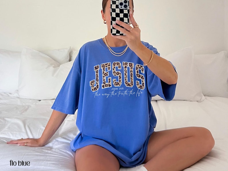 May include: A blue t-shirt with the word "JESUS" in a leopard print design across the chest. The text "the way the truth the life" is below the word "JESUS". The shirt is a relaxed fit.