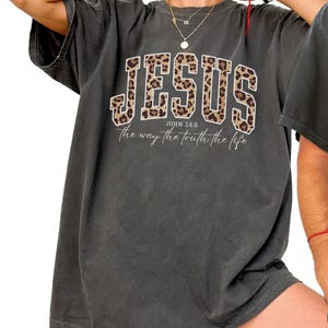 May include: Dark gray t-shirt with the word "JESUS" in a leopard print design. The text "JOHN 14:6" and "the way the truth the life" are printed below the word "JESUS".