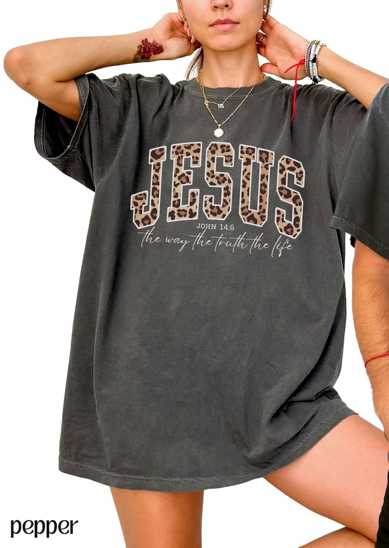 May include: Dark gray t-shirt with the word "JESUS" in a leopard print design. The text "JOHN 14:6" and "the way the truth the life" are printed below the word "JESUS".